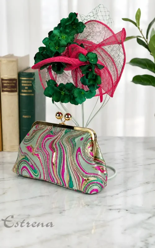 Tocado fucsia con flores verdes y redecilla junto a bolso de mano con estampado psicodélico en Estrena Moda Cartagena.