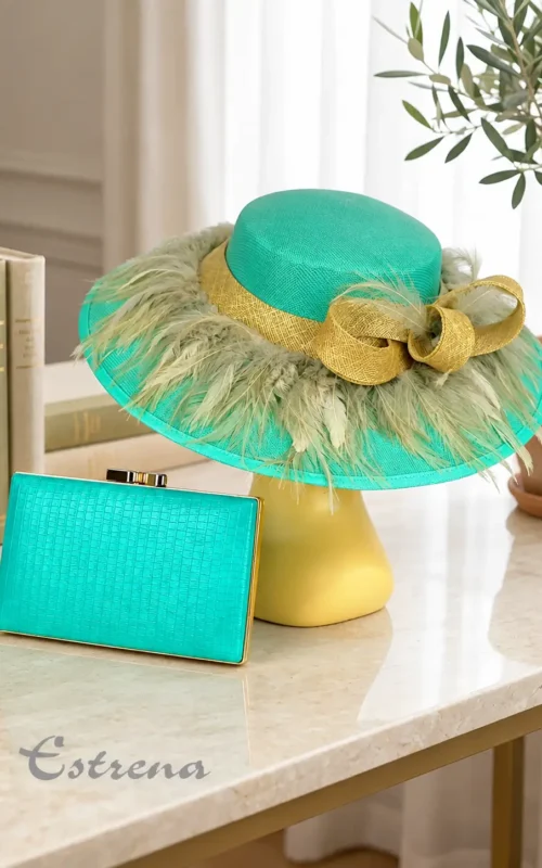 Pamela verde turquesa con plumas y lazo dorado junto a bolso clutch rígido en Estrena Moda Cartagena.