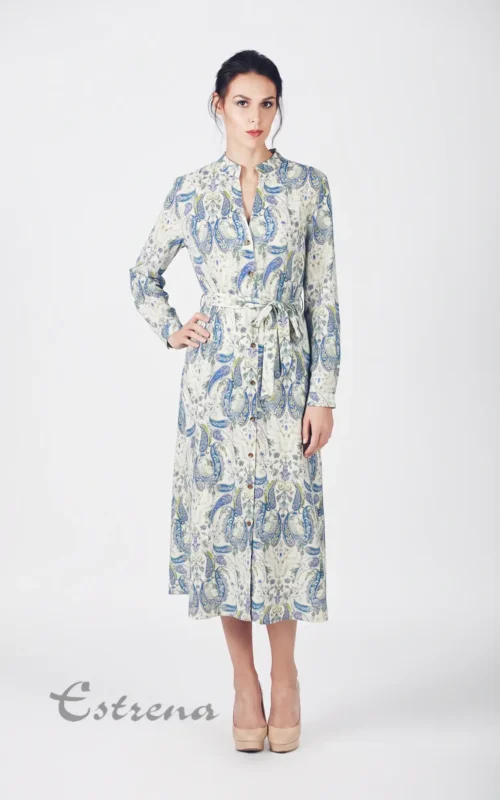 Mujer posando con vestido largo camisero de manga larga y estampado de cachemira azul sobre fondo crema.