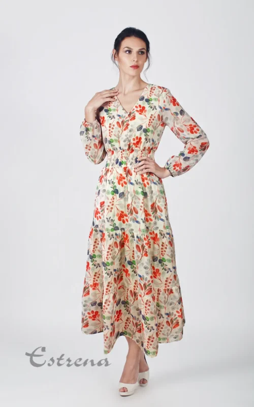 Mujer posando con un vestido largo de manga larga con estampado botánico rojo y verde sobre fondo crema.