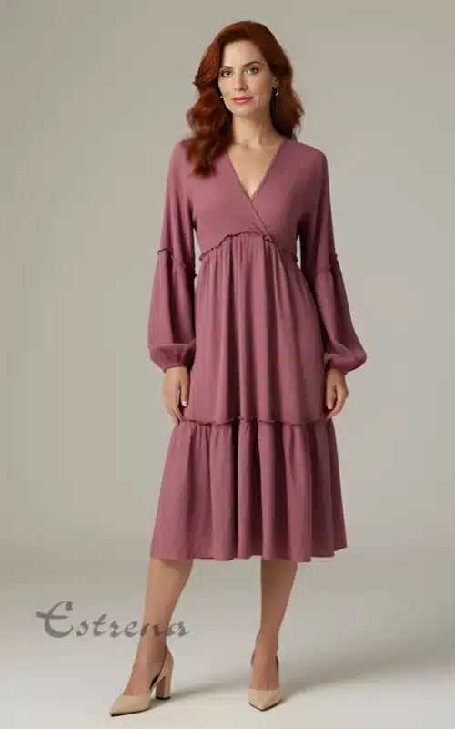 Mujer posando con vestido midi de manga larga color rosa viejo con escote cruzado y falda con volantes.
