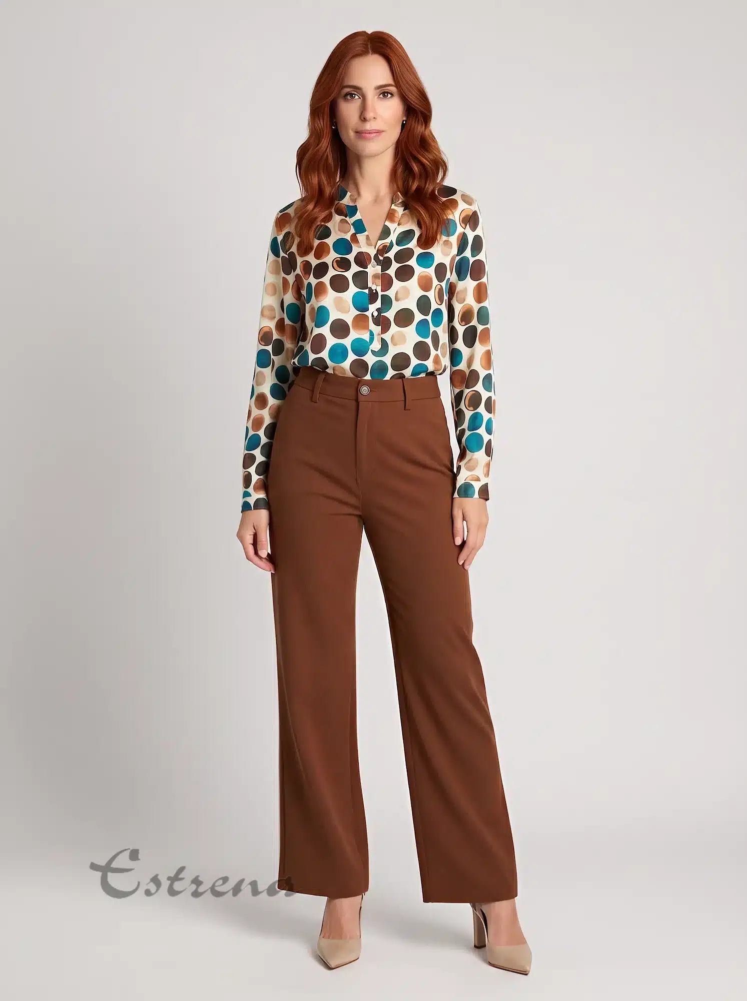 Mujer pelirroja vistiendo blusa satinada de lunares en tonos marrones y azules combinada con pantalón marrón de pinzas.