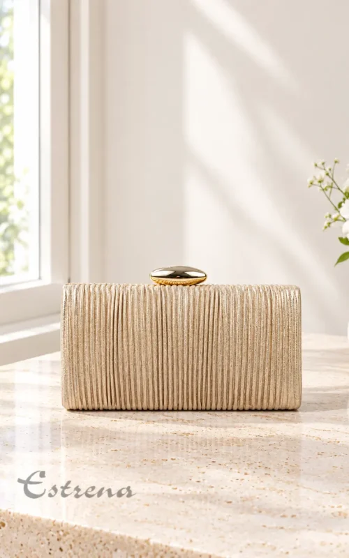 Bolso de fiesta tipo clutch rígido dorado con textura plisada vertical y broche superior dorado sobre una mesa de mármol.