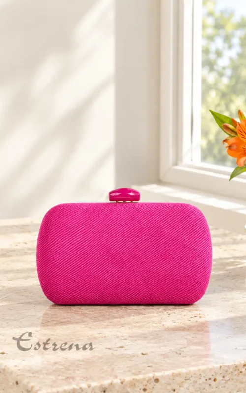 Bolso de fiesta tipo clutch rígido fucsia con textura entrelazada diagonal sobre superficie de mármol de Estrena Moda Cartagena.