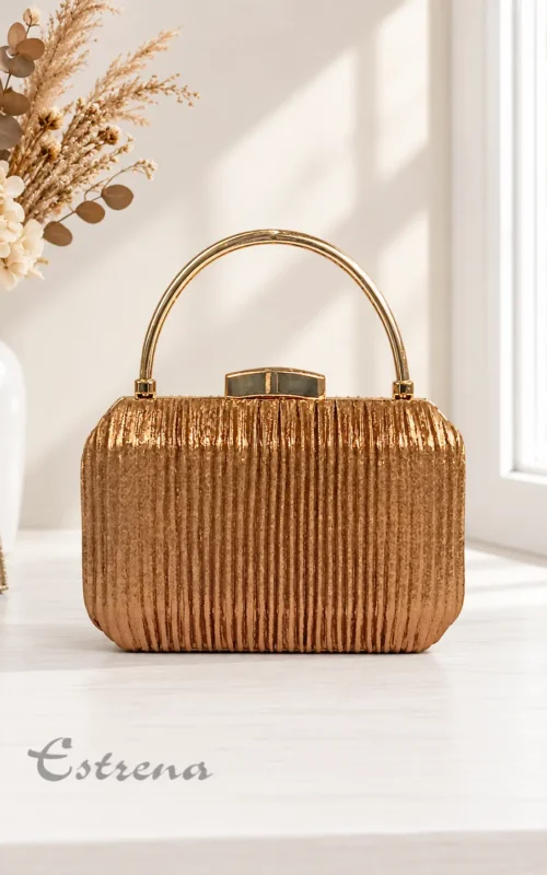 Bolso de fiesta estilo clutch rígido plisado en color bronce metalizado con asa superior dorada sobre una mesa blanca