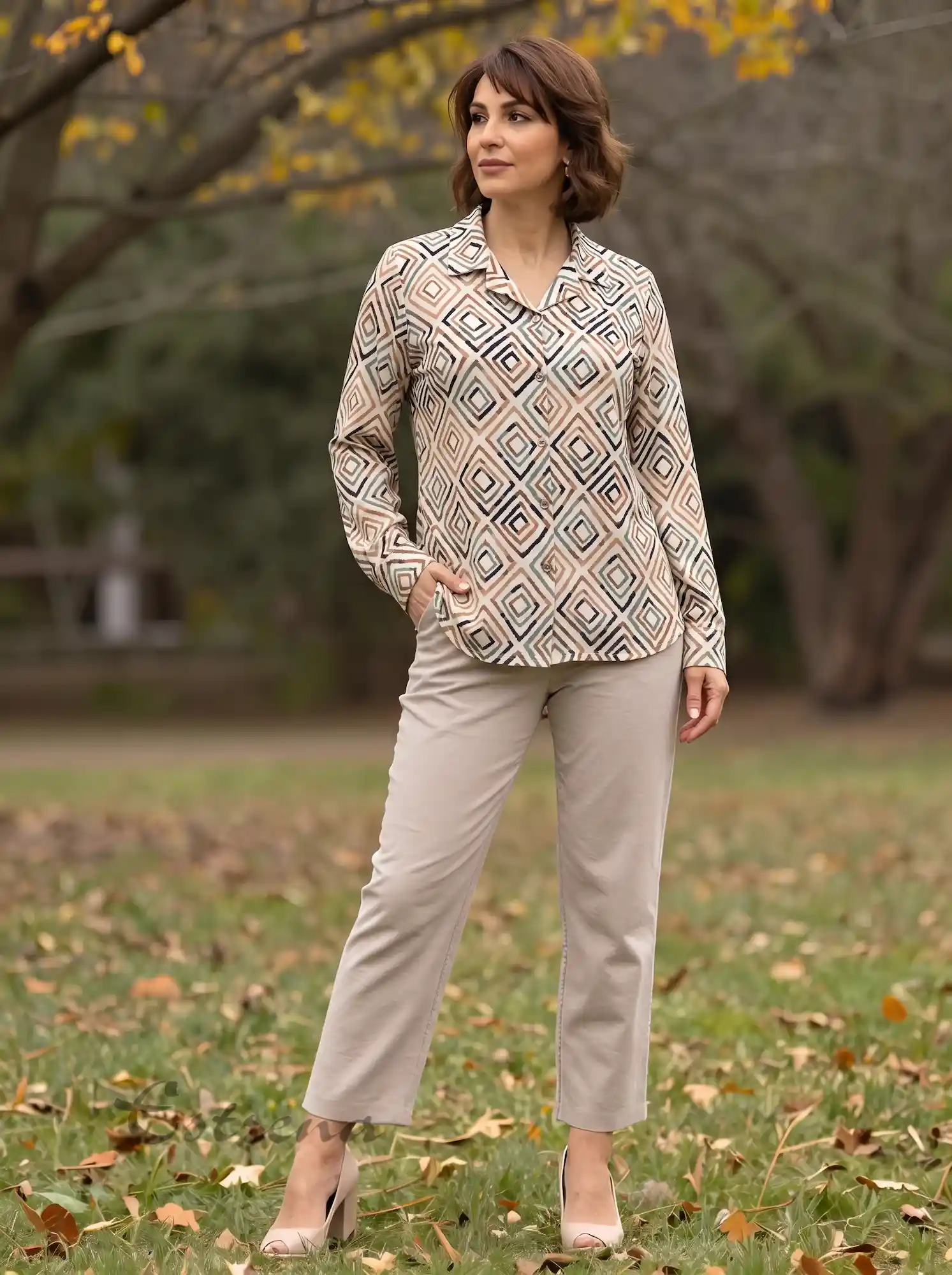 Mujer posando en un parque con una camisa de manga larga con estampado geométrico beige y marrón de Estrena Moda.
