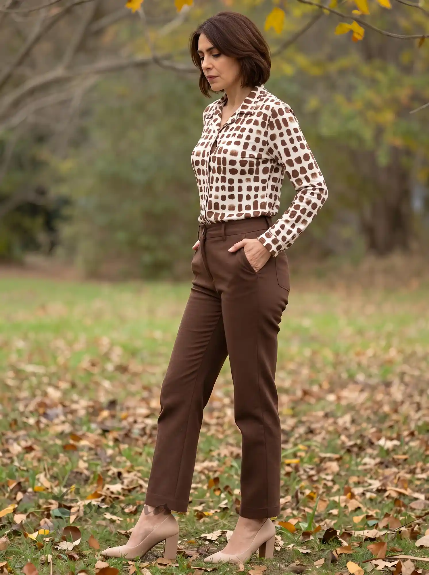 Mujer de perfil vistiendo una camisa estampada beige y marrón metida por dentro del pantalón en Estrena Moda.