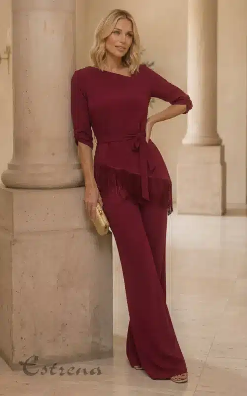 Mujer posando junto a una columna con un conjunto de fiesta color burdeos de pantalón palazzo y top con flecos.