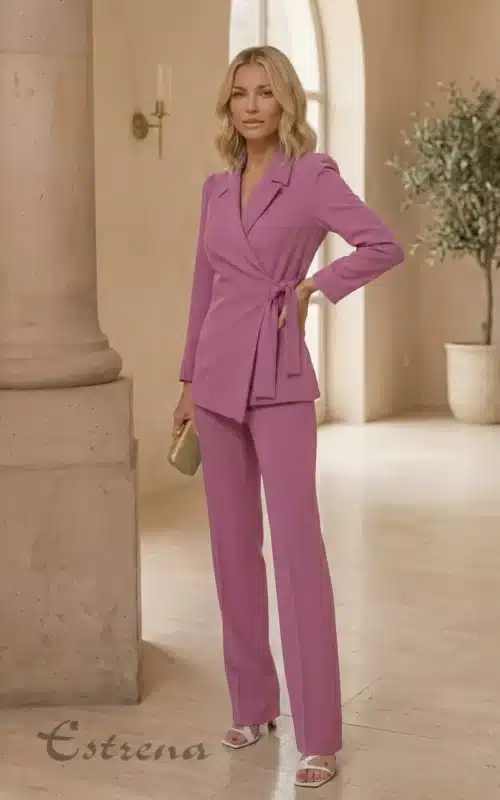 Modelo rubia posando con traje de chaqueta cruzada malva, pantalón recto a juego y bolso de mano dorado metálico.