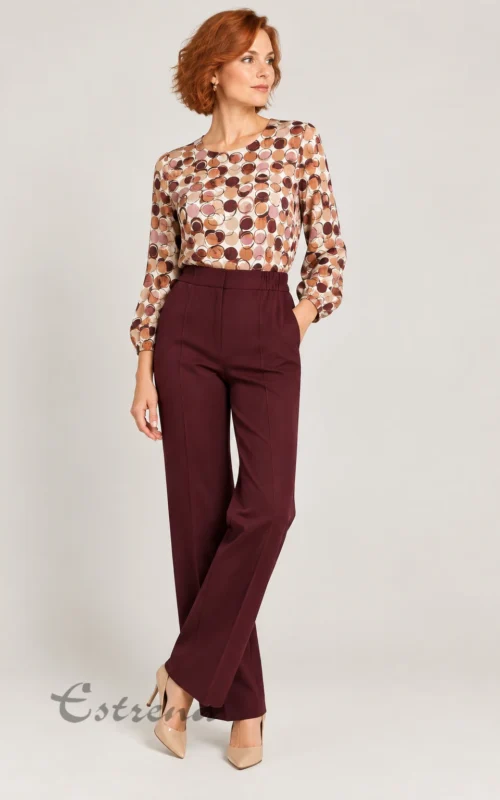 Mujer vistiendo un pantalón de vestir granate de tiro alto combinado con blusa estampada y zapatos de tacón beige.