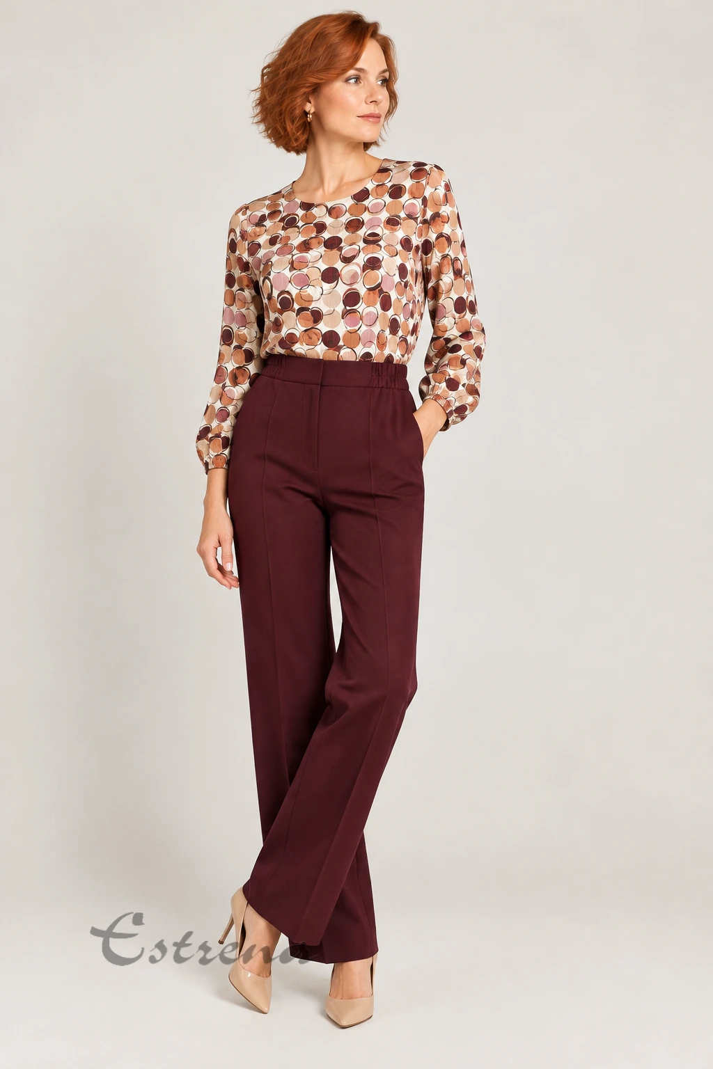 Mujer vistiendo un pantalón de vestir granate de tiro alto combinado con blusa estampada y zapatos de tacón beige.