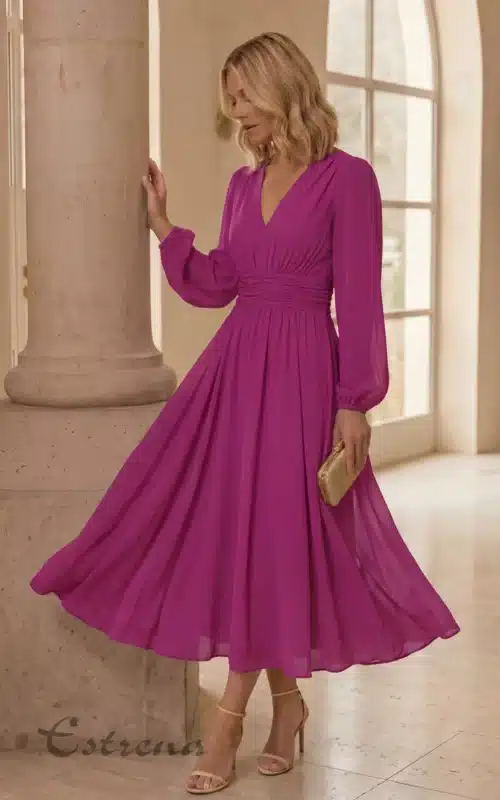Mujer rubia con vestido midi buganvilla de manga larga, falda con vuelo, bolso dorado y sandalias de tacón.