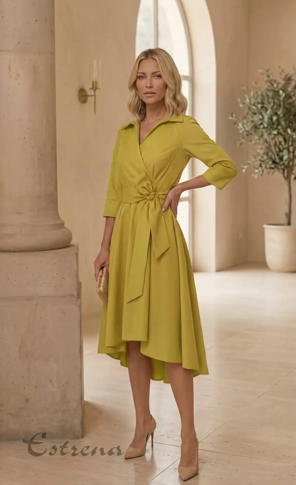 Mujer rubia con vestido midi camisero cruzado color amarillo mostaza con lazo y zapatos de tacón nude en un gran salón.