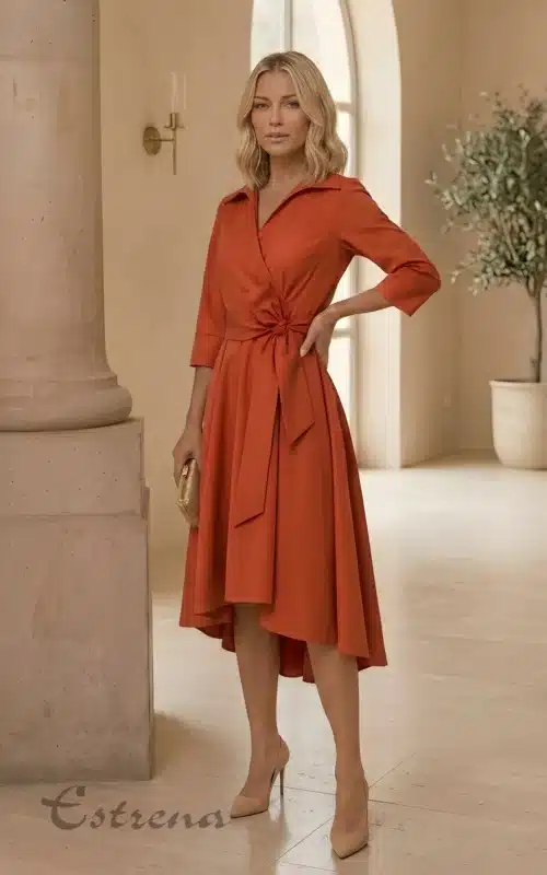 Mujer rubia con vestido midi camisero cruzado color teja con lazo y zapatos de tacón nude en un salón luminoso.
